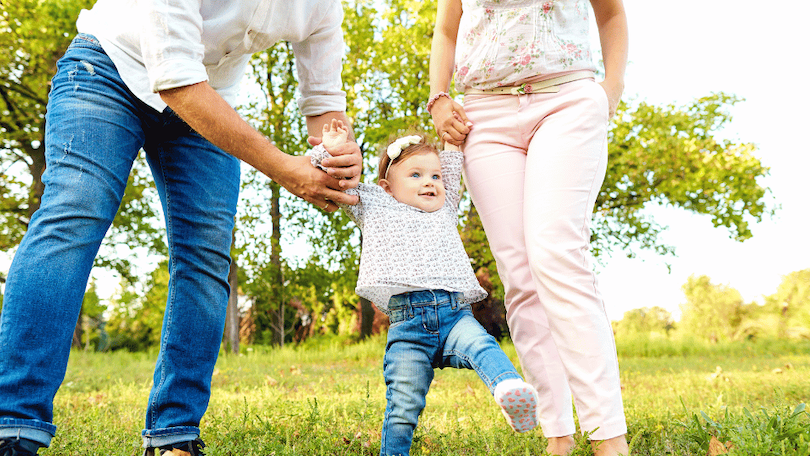baby-walking-outside-with-parents-in-greenery