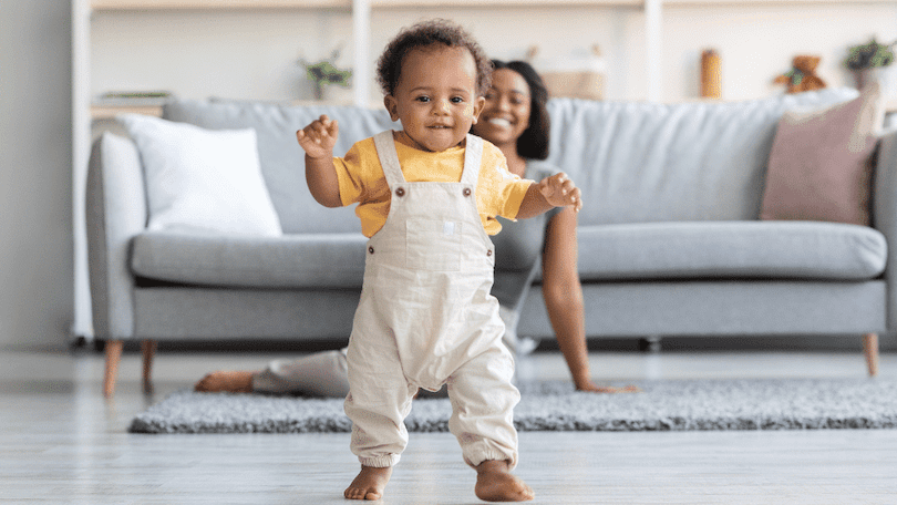 cute-dark-skinned-baby-learning-to-walk-with-mom-smiling-in-background